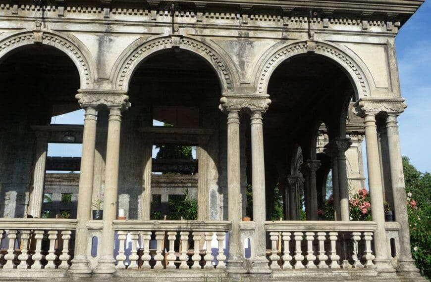 The Ruins, in silay, bacolod. The arches form a covered walkway or verandah. This sight is a must-see for any Bacolod travel guide. The structure is partially in ruins with visible greenery in the background and potted plants along the balustrade.