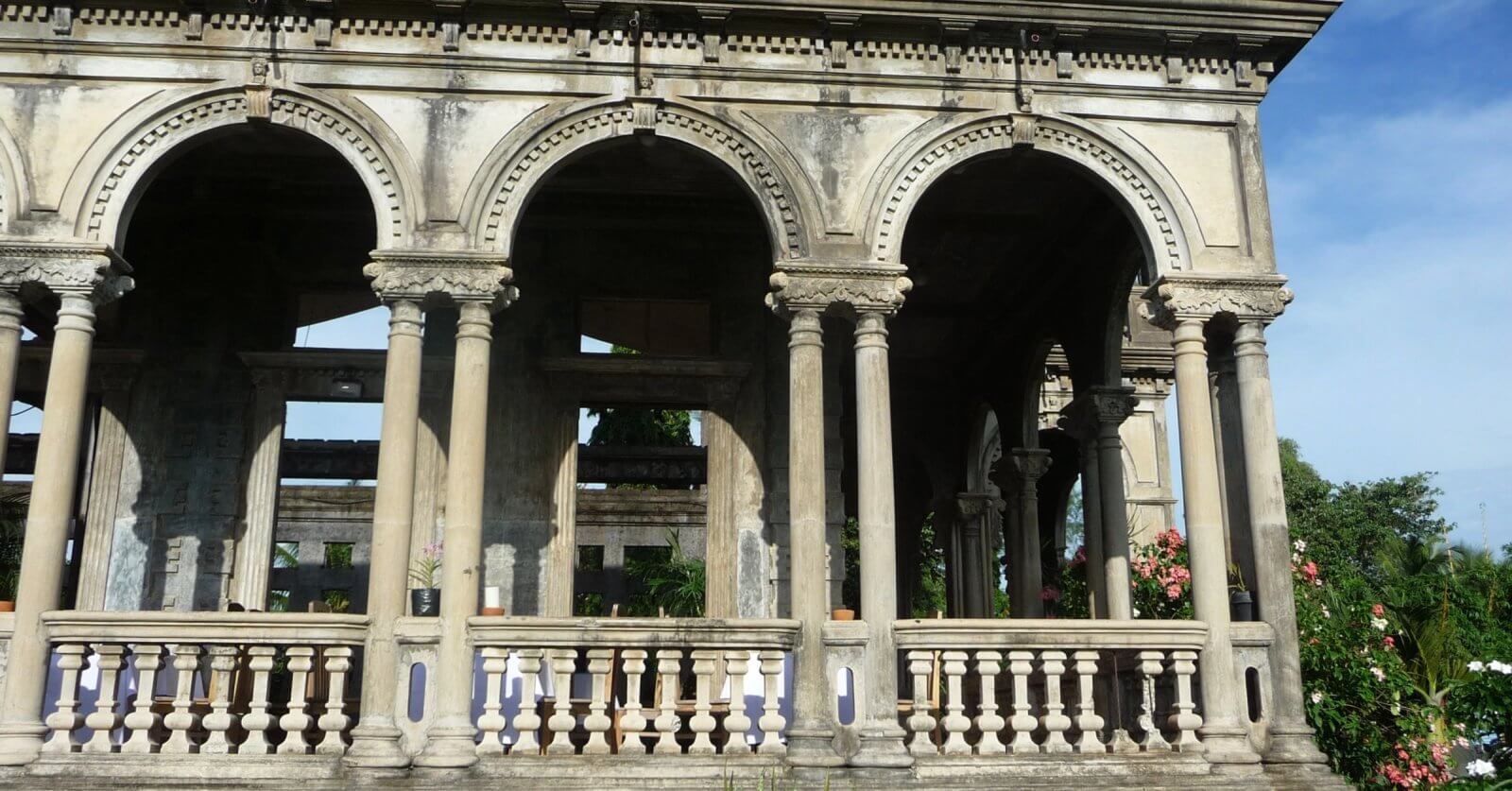 The Ruins, in silay, bacolod. The arches form a covered walkway or verandah. This sight is a must-see for any Bacolod travel guide. The structure is partially in ruins with visible greenery in the background and potted plants along the balustrade.