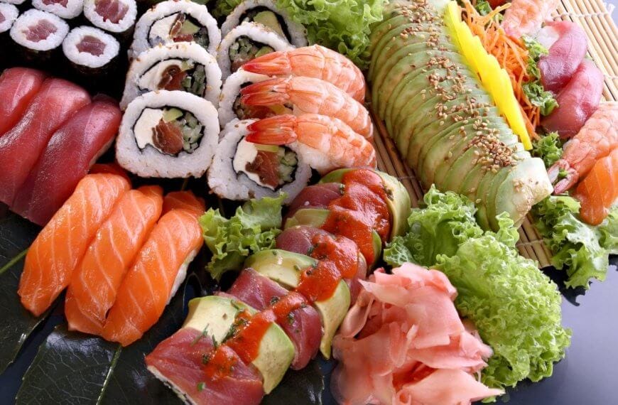 A colorful sushi platter displayed artfully at Okada Manila, one of the best restaurants. The assortment includes culinary gems like nigiri sushi with salmon and tuna, various sushi rolls with fillings like vegetables and seafood topped with avocado and sauces, shrimp, garnished with ginger, wasabi and lettuce.