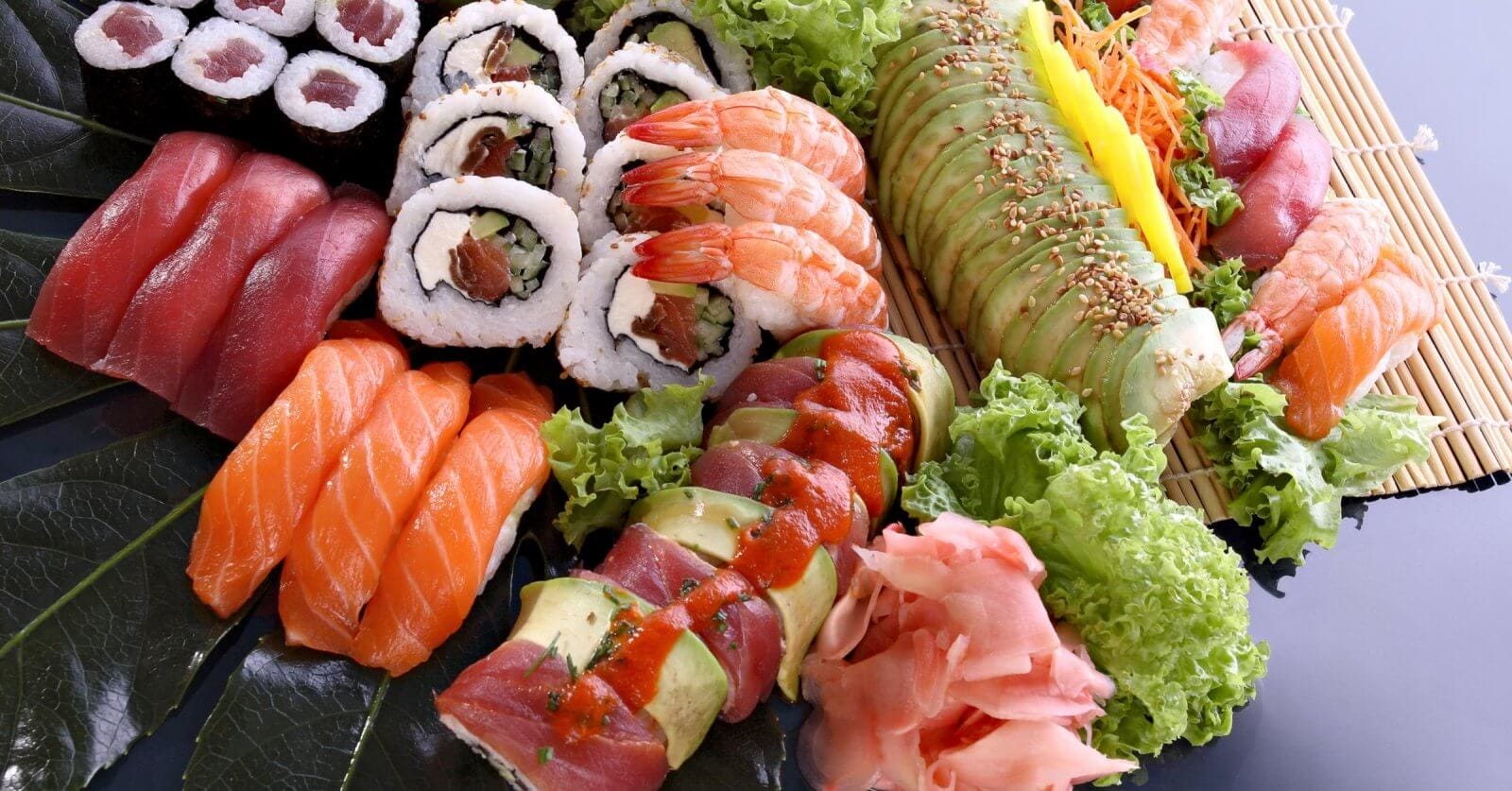 A colorful sushi platter displayed artfully at Okada Manila, one of the best restaurants. The assortment includes culinary gems like nigiri sushi with salmon and tuna, various sushi rolls with fillings like vegetables and seafood topped with avocado and sauces, shrimp, garnished with ginger, wasabi and lettuce.