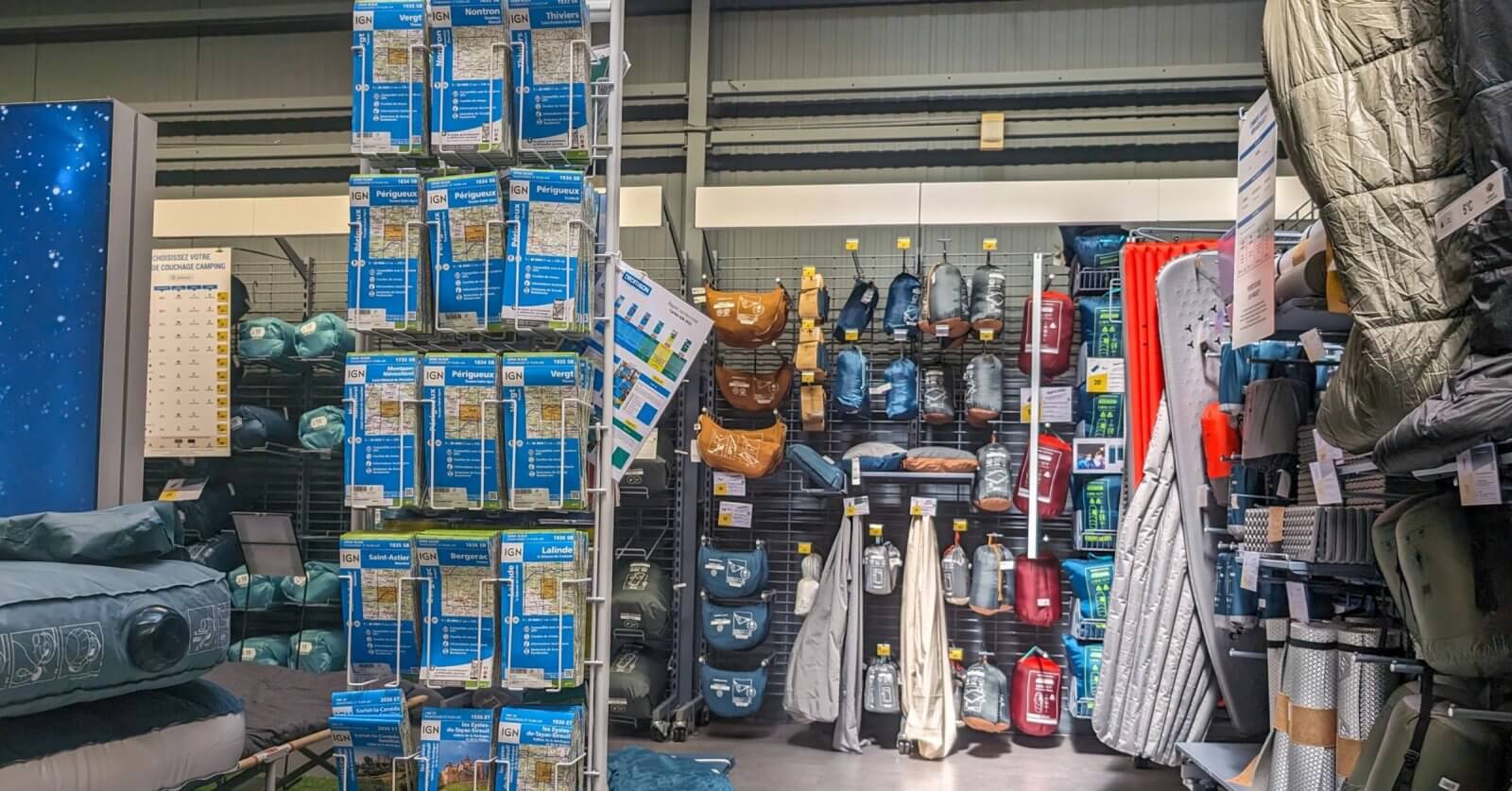 A well-organized camping gear section in one of the best camping stores in Metro Manila displays an array of neatly arranged outdoor equipment. On the left, air mattresses and travel pillows are stacked on shelves. The center showcases various hydration packs and bags. The right features sleeping bags and camping mats hanging on hooks.