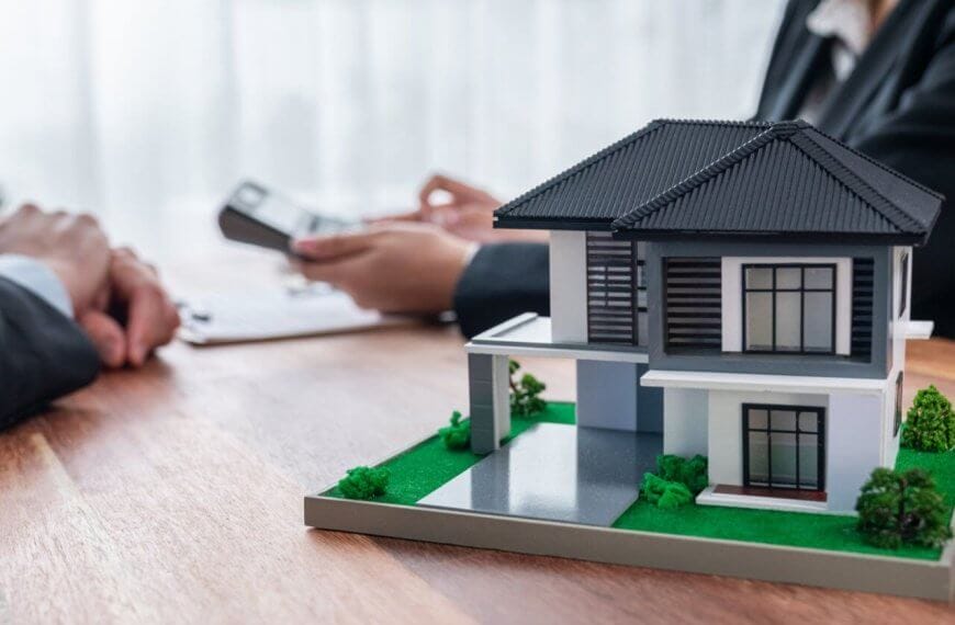 Two individuals in business suits are seated at the table, one holding a clipboard and the other engaging in discussion about the housing loan, indicating a professional meeting, about real estate.