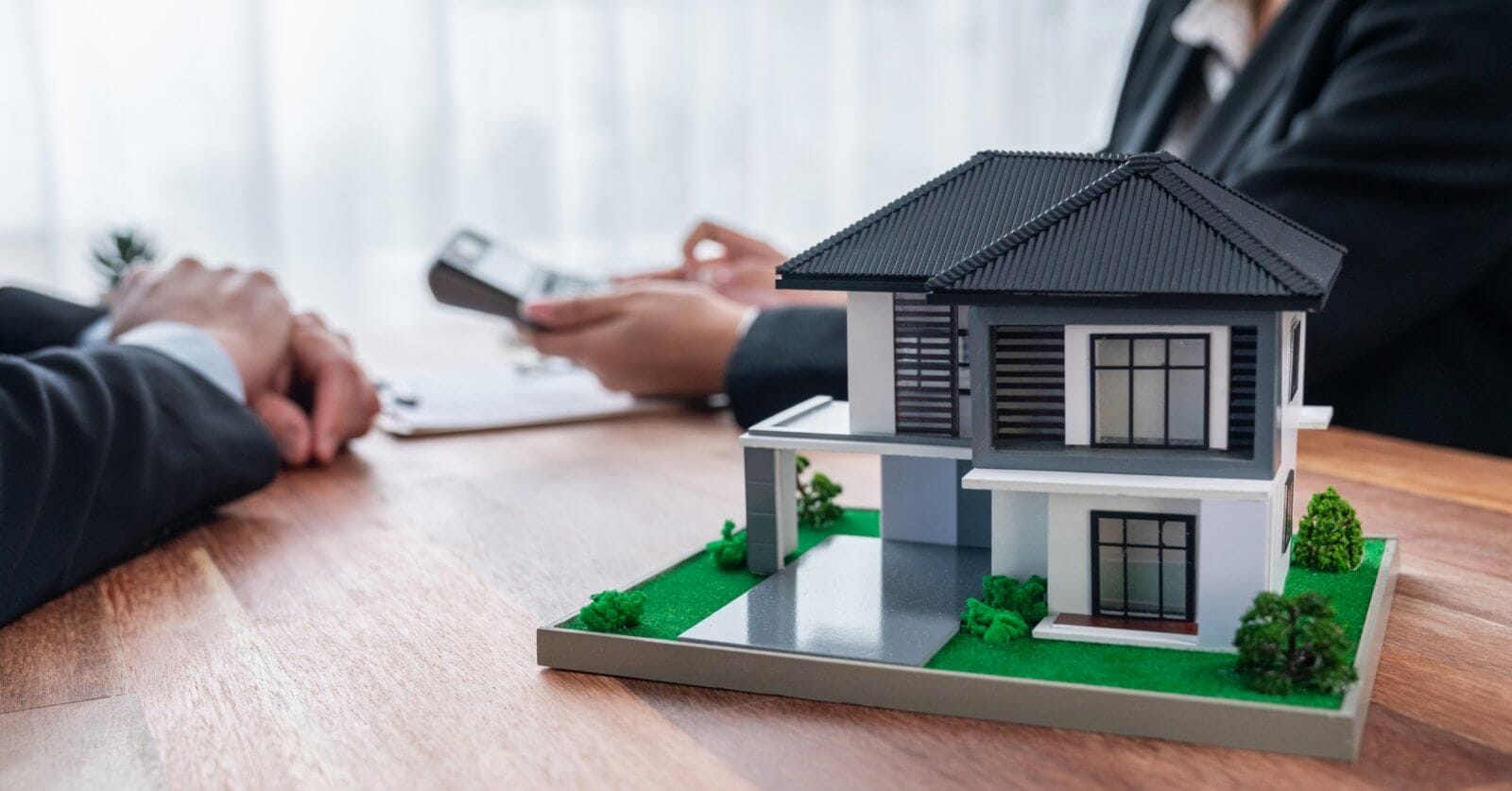 Two individuals in business suits are seated at the table, one holding a clipboard and the other engaging in discussion about the housing loan, indicating a professional meeting, about real estate.