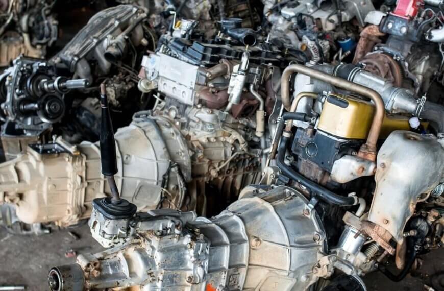 A cluttered workshop in Metro Manila with multiple disassembled car engines and gearboxes. The engines are placed close together on the floor, showing components like turbochargers, exhaust manifolds, and fuel injection systems. Some tools and small parts from the 35 Best Junk Shops are scattered around the area.