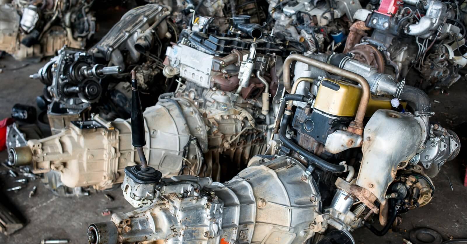 A cluttered workshop in Metro Manila with multiple disassembled car engines and gearboxes. The engines are placed close together on the floor, showing components like turbochargers, exhaust manifolds, and fuel injection systems. Some tools and small parts from the 35 Best Junk Shops are scattered around the area.