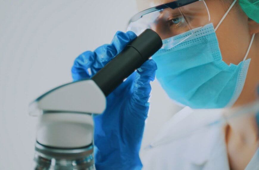 A pathologist wearing a protective face mask, goggles, and blue gloves, is closely examining a sample through a microscope. The technician's focus is evident as they work in a well-lit, sterile environment. This image highlights the meticulous scientific research and expert care one can expect from the best pathologists in Metro Manila.
