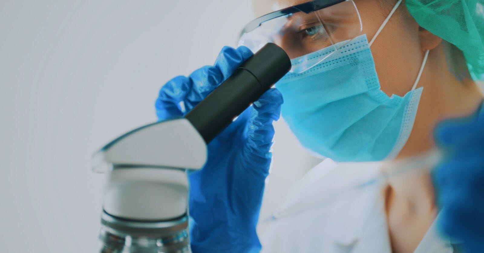 A pathologist wearing a protective face mask, goggles, and blue gloves, is closely examining a sample through a microscope. The technician's focus is evident as they work in a well-lit, sterile environment. This image highlights the meticulous scientific research and expert care one can expect from the best pathologists in Metro Manila.