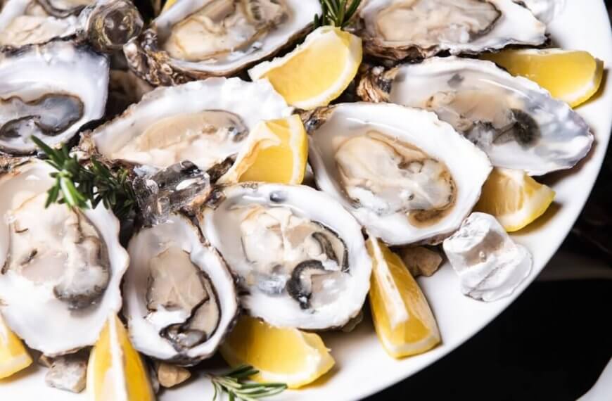 A must-try dish at one of the top restaurants in Gateway Mall, this plate of half-shell oysters is garnished with lemon wedges and sprigs of rosemary. Nestled on a bed of crushed ice, the oysters display their smooth, creamy texture and varying shades of gray, accented by vibrant citrus and herbs.