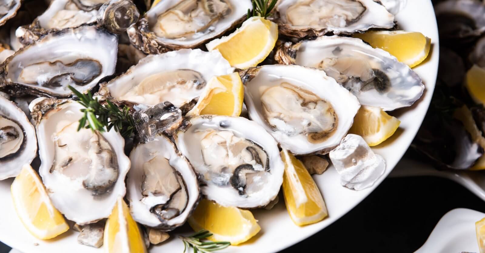 A must-try dish at one of the top restaurants in Gateway Mall, this plate of half-shell oysters is garnished with lemon wedges and sprigs of rosemary. Nestled on a bed of crushed ice, the oysters display their smooth, creamy texture and varying shades of gray, accented by vibrant citrus and herbs.
