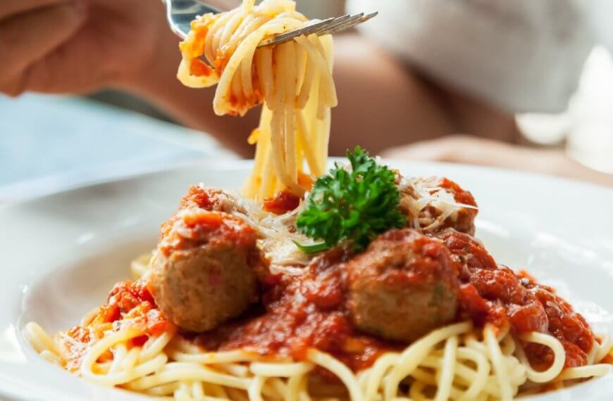 spaghetti topped with red tomato sauce, meatballs, grated cheese, and a sprig of parsley. A person is twirling the pasta around a fork, with the focus on the forkful of spaghetti being lifted from the plate at one of BGC's 46 Must-Try Restaurants near SM Aura.
