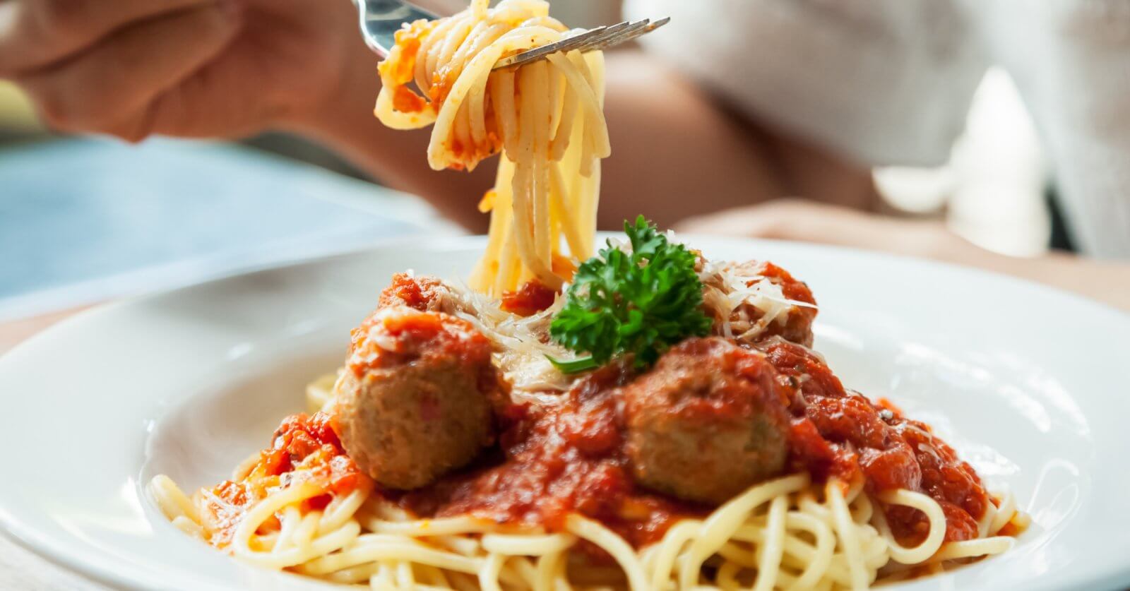 spaghetti topped with red tomato sauce, meatballs, grated cheese, and a sprig of parsley. A person is twirling the pasta around a fork, with the focus on the forkful of spaghetti being lifted from the plate at one of BGC's 46 Must-Try Restaurants near SM Aura.