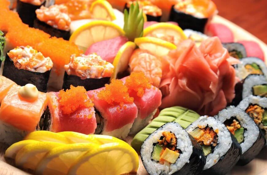 A wooden platter from sulit eats at SM Dasmariñas is filled with a variety of colorful sushi rolls and sashimi. The assortment includes rolls topped with salmon, tuna, roe, and avocado, alongside garnishes of lemon slices, pickled ginger, and wasabi. The presentation is vibrant and visually appealing.