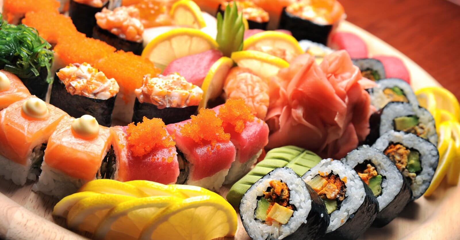 A wooden platter from sulit eats at SM Dasmariñas is filled with a variety of colorful sushi rolls and sashimi. The assortment includes rolls topped with salmon, tuna, roe, and avocado, alongside garnishes of lemon slices, pickled ginger, and wasabi. The presentation is vibrant and visually appealing.