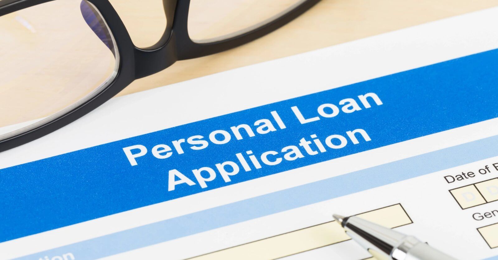 A close-up of a Sulit personal loan application form with a blue header. "Personal Loan Application" is prominently displayed. There's a pen on the form, and a pair of glasses is partially visible in the upper left corner. The form includes fields to fill in personal details alongside the convenient use of a loan calculator.