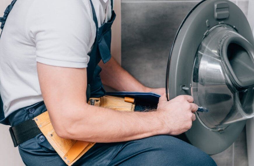 A person repairing a front-loading washing machine in Metro Manila. With a yellow tool belt brimming with various tools around their waist, they are closely examining the open door of the washing machine, appearing focused on providing top-notch Washing Machine Repair Services.