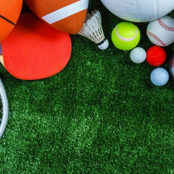 A variety of sports equipment arranged on a green grass surface. Items include a basketball, yoga mat, American football, soccer ball, badminton birdie, table tennis paddle, baseball glove, tennis ball, golf balls, cricket bat. Perfect for enthusiasts in Metro Manila's sports centers.