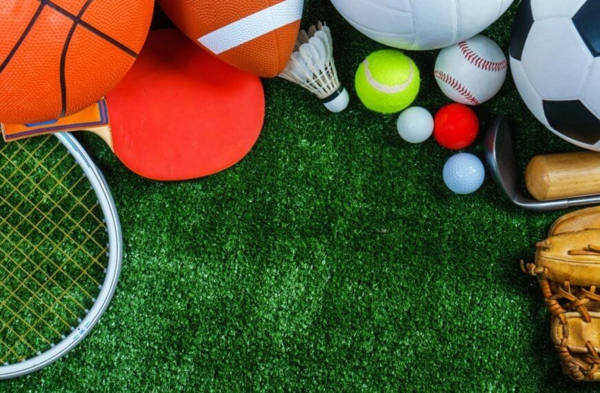 A variety of sports equipment arranged on a green grass surface. Items include a basketball, yoga mat, American football, soccer ball, badminton birdie, table tennis paddle, baseball glove, tennis ball, golf balls, cricket bat. Perfect for enthusiasts in Metro Manila's sports centers.