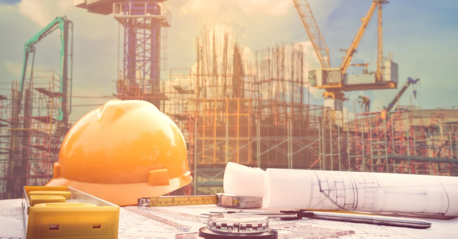 A construction site with cranes and scaffolding rises under Manila's blue sky. In the foreground, a yellow hard hat, rolled blueprints, a measuring tape, and a compass rest on a table, symbolizing architectural planning backed by construction supply companies known for quality and reliability.