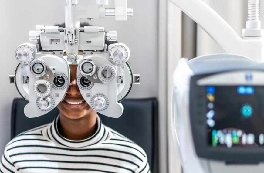 In one of Metro Manila's best eye clinics, a person in a striped shirt sits behind a phoropter, undergoing an eye examination. The focus is on the device with its various dials and lenses, while a blurred vision-testing machine looms in the foreground. The scene is set in a bright, clinical room.