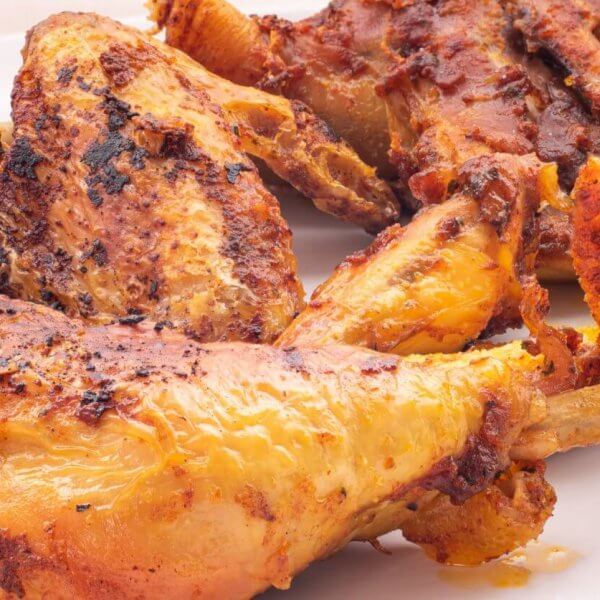 The best-grilled, seasoned chicken pieces with a golden-brown crust are served on a white plate. Perfectly charred for that flame-grilled texture, they're infused with visible spices and boast a juicy appearance. This appetizing dish would be right at home in Pangasinan's top restaurants.