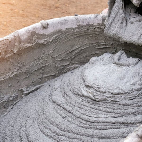 A close-up of wet cement being poured into a wheelbarrow from a mixer, forming a swirling pattern with rough texture. The wheelbarrow is slightly stained, echoing the bustling construction sites in Metro Manila, where dirt and cement suppliers ensure seamless progress amidst splatters.