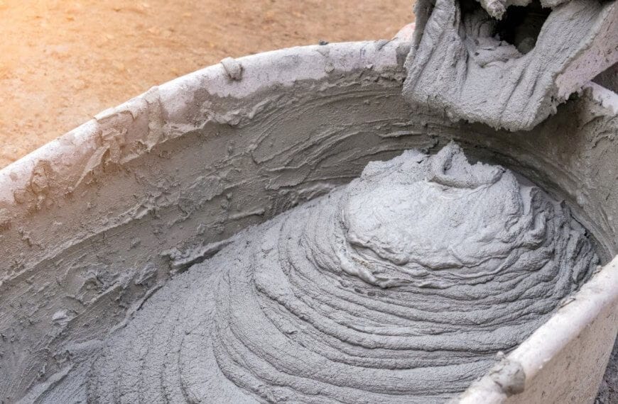 A close-up of wet cement being poured into a wheelbarrow from a mixer, forming a swirling pattern with rough texture. The wheelbarrow is slightly stained, echoing the bustling construction sites in Metro Manila, where dirt and cement suppliers ensure seamless progress amidst splatters.