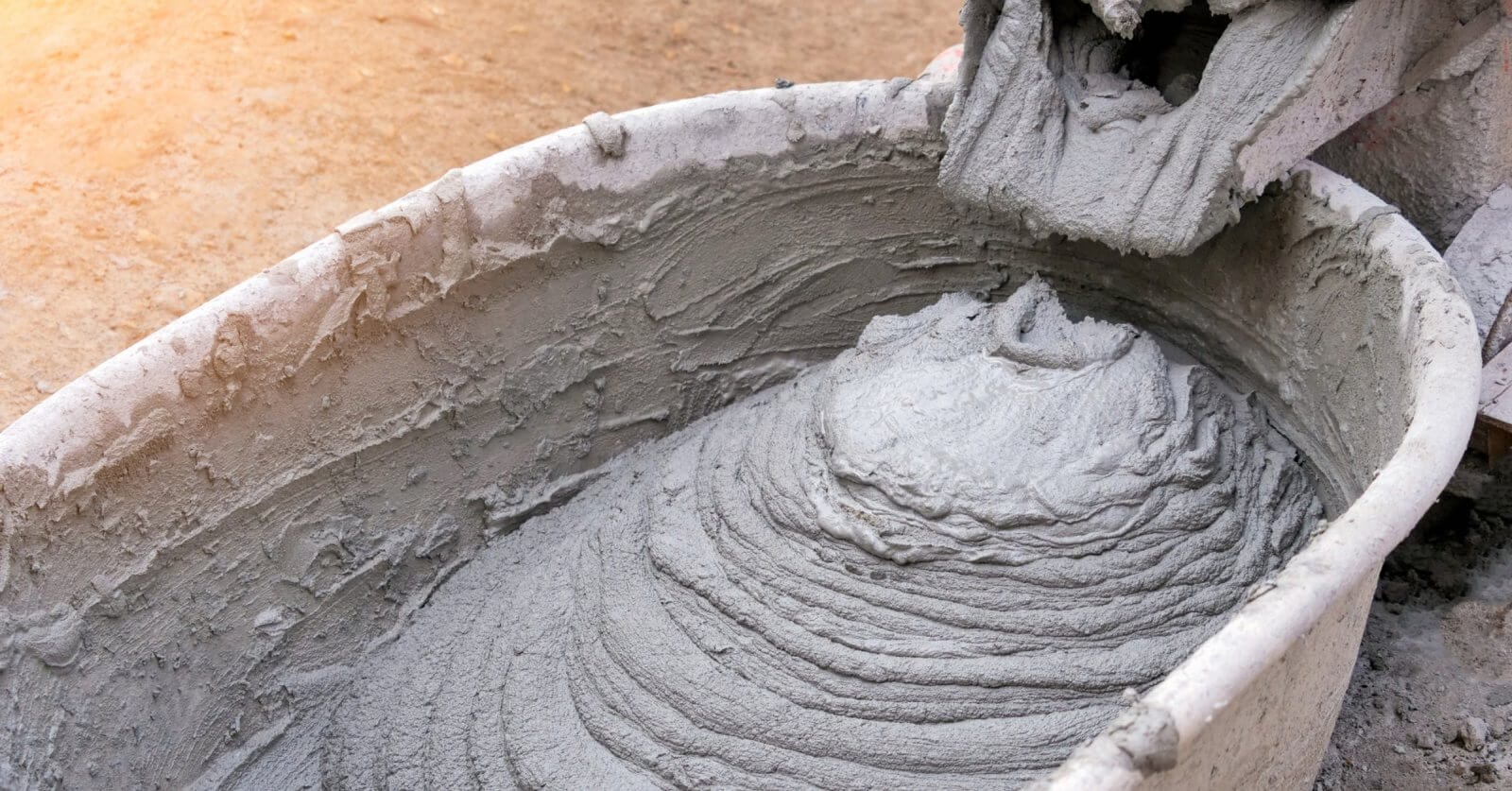 A close-up of wet cement being poured into a wheelbarrow from a mixer, forming a swirling pattern with rough texture. The wheelbarrow is slightly stained, echoing the bustling construction sites in Metro Manila, where dirt and cement suppliers ensure seamless progress amidst splatters.