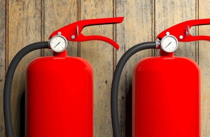 Two bright red fire extinguishers with black hoses and pressure gauges are mounted against a rustic wooden wall in Manila. The sleek, vibrant red of the extinguishers contrasts with the natural wood texture, while suppliers ensure timely fire extinguisher refills to maintain safety standards.