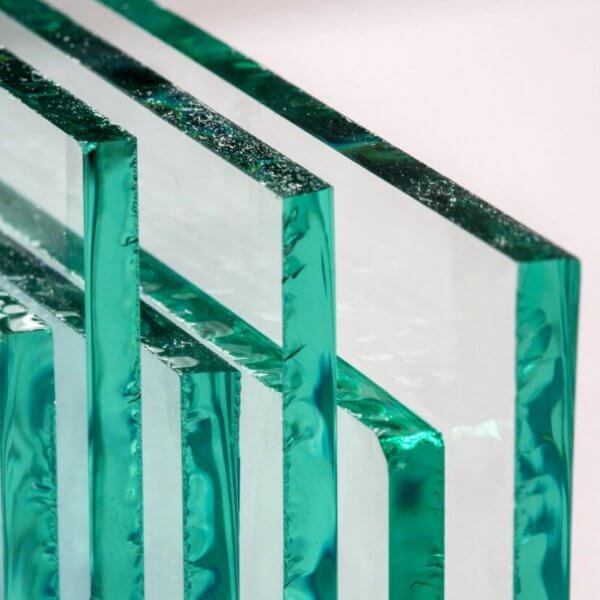 Close-up of four rectangular glass panes, supplied by leading glass suppliers in Metro Manila, standing upright and lined up horizontally against a neutral background. The edges show a green tint, with surfaces reflecting light to create a layered, transparent effect that highlights the clarity and texture.