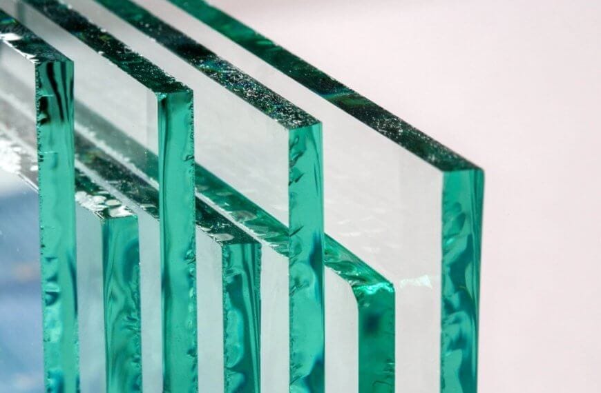 Close-up of four rectangular glass panes, supplied by leading glass suppliers in Metro Manila, standing upright and lined up horizontally against a neutral background. The edges show a green tint, with surfaces reflecting light to create a layered, transparent effect that highlights the clarity and texture.