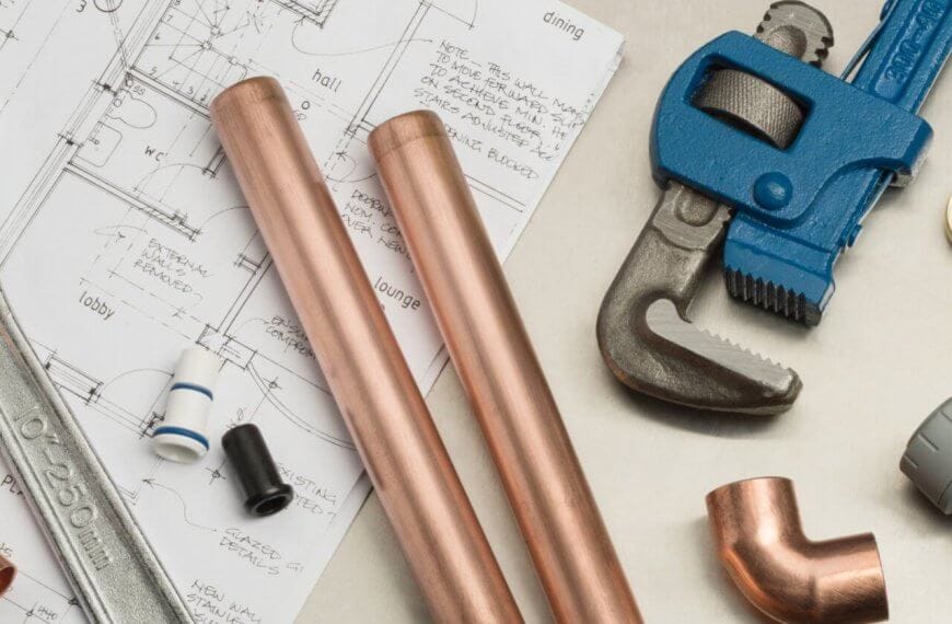 Plumbing tools and materials, ideal for plumbing services in Metro Manila, are neatly arranged on an architectural blueprint. Items include a large adjustable wrench, two copper pipes, a blue pipe wrench, copper fittings, and various pipe components set against detailed floor plans and elevations.