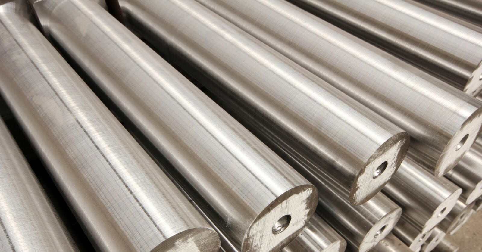 Close-up of several smooth, cylindrical metal rods stacked in parallel rows. Sourced from the best steel suppliers, these rods have a shiny, reflective surface and consistent diameter. Each rod has a small central hole at one end, adding a pattern to the otherwise uniform texture.