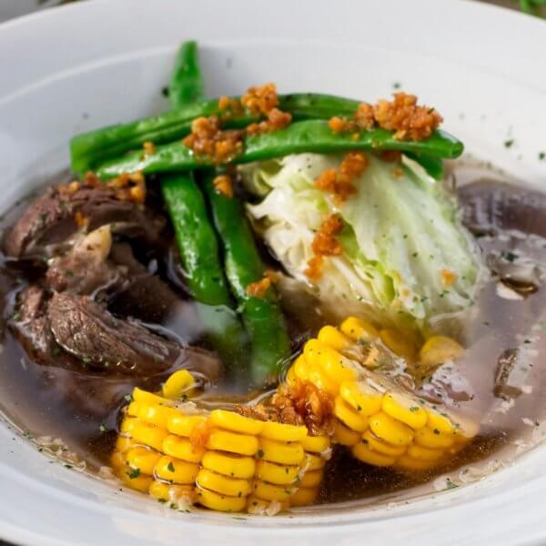 A bowl of the best soup in Batangas City, featuring tender beef, sweet corn, crisp cabbage, and fresh green beans in a clear broth, offers a delightful taste that local restaurants proudly serve.