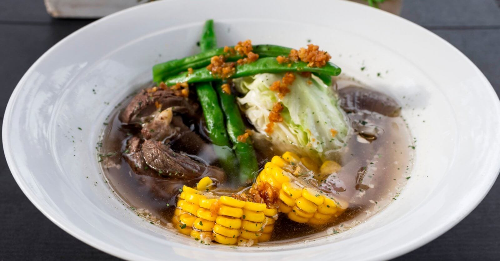 A bowl of the best soup in Batangas City, featuring tender beef, sweet corn, crisp cabbage, and fresh green beans in a clear broth, offers a delightful taste that local restaurants proudly serve.