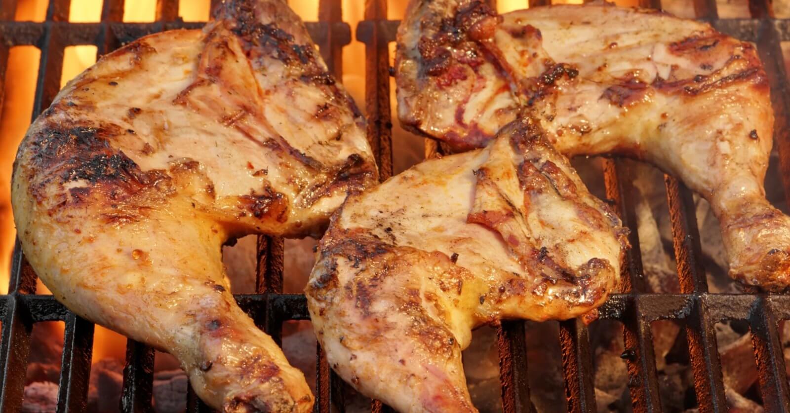 Three seasoned chicken leg quarters are grilling over open flames with visible char marks much like the sizzle you might find in a vibrant commercial space in Iligan City where local flavors blend with culinary artistry
