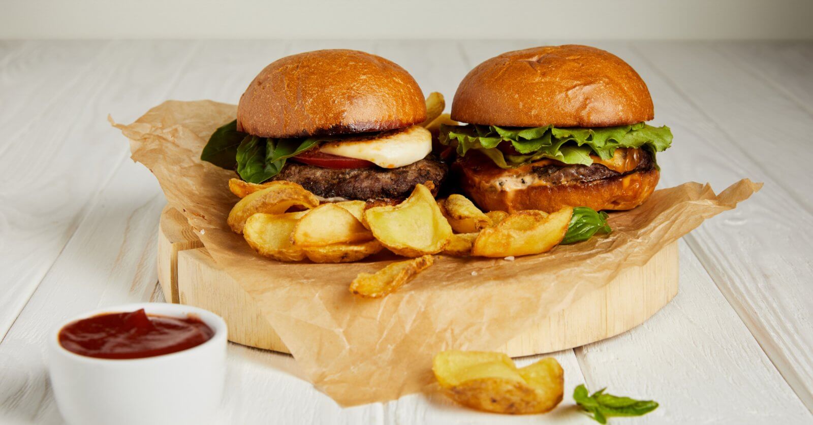 Two burgers with lettuce and cheese sit enticingly on a wooden board accompanied by crispy curly fries and a cup of ketchupa perfect meal to enjoy in one of Iligan Citys vibrant commercial spaces
