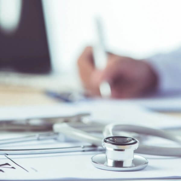 Close-up of a stethoscope and an infectious disease physician's hand writing on a clipboard, with a prescription pad in the background. This snapshot captures the dedication of one of Metro Manila's best medical professionals.