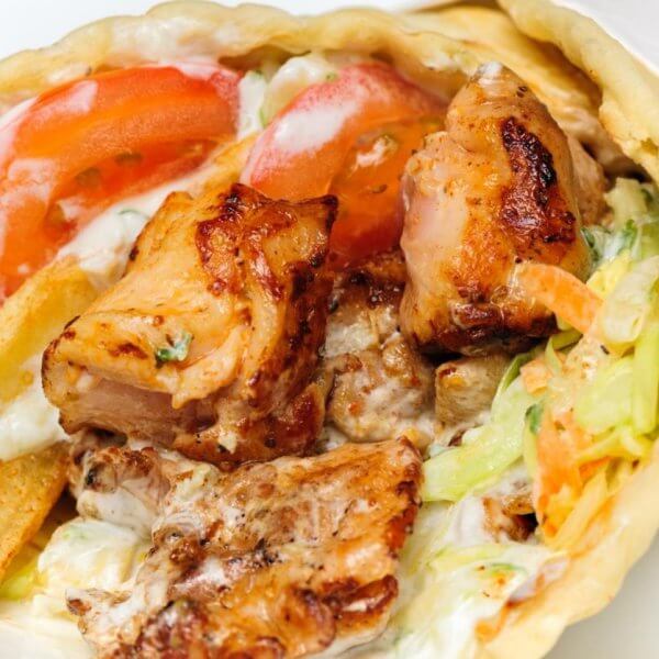 Close-up of a chicken wrap with grilled meat, lettuce, tomatoes, fries, and creamy sauce, wrapped in flatbread—one of the 23 Best dishes you'll find at top restaurants in Marawi City.