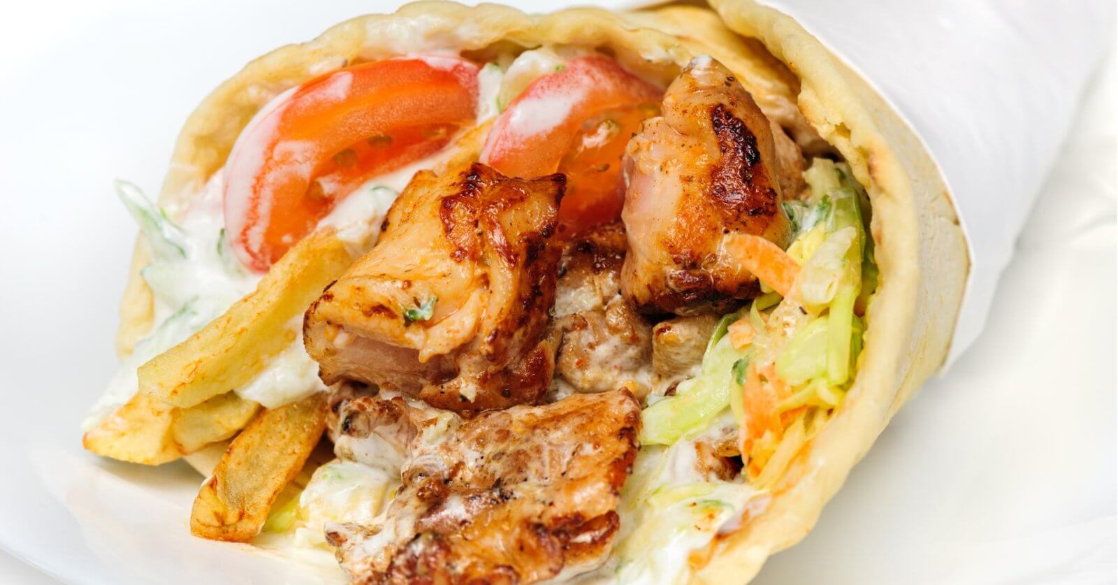 Close-up of a chicken wrap with grilled meat, lettuce, tomatoes, fries, and creamy sauce, wrapped in flatbread—one of the 23 Best dishes you'll find at top restaurants in Marawi City.