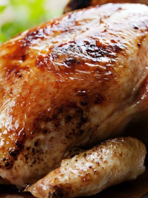 Golden roasted chicken on a wooden board with herbs, reminiscent of the savory delights you'd find at the best restaurants around. A knife is placed beside it, ready to carve into this culinary masterpiece.