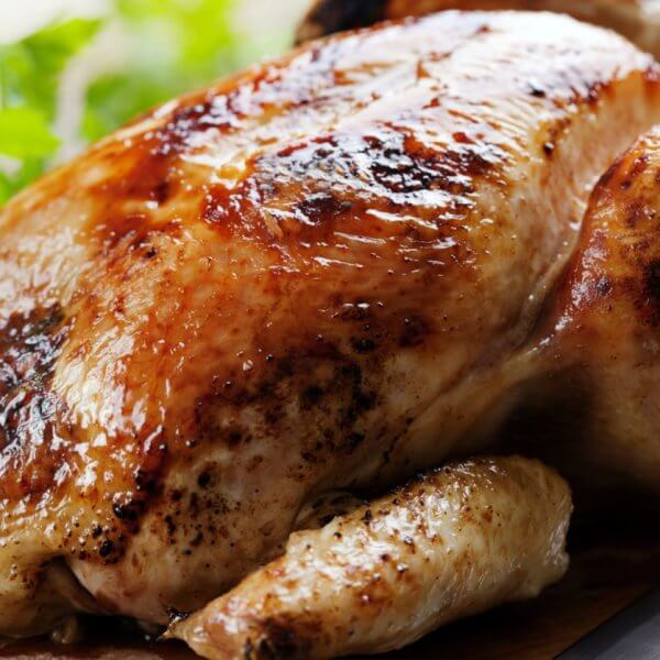 Golden roasted chicken on a wooden board with herbs, reminiscent of the savory delights you'd find at the best restaurants around. A knife is placed beside it, ready to carve into this culinary masterpiece.