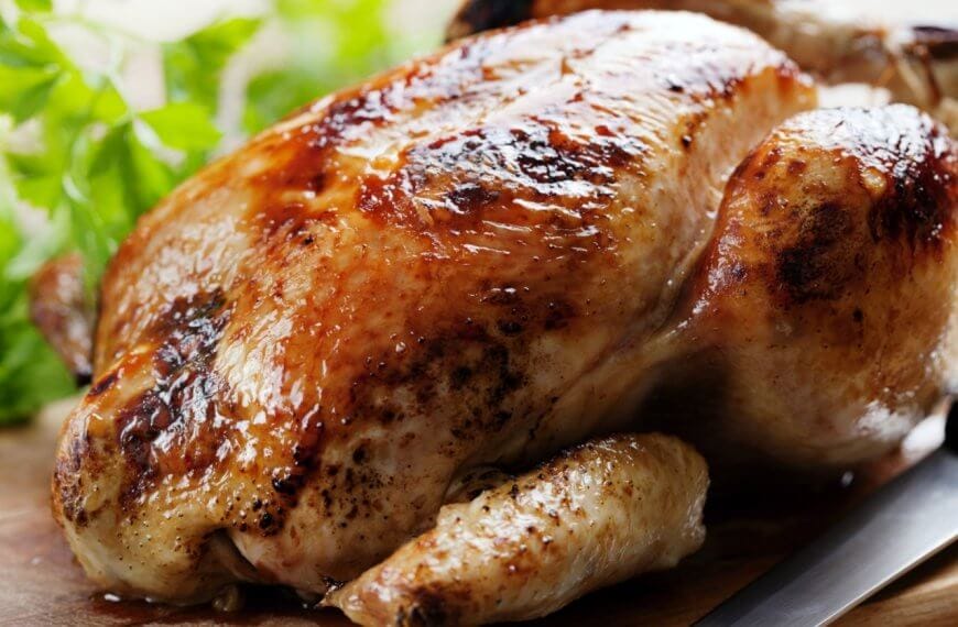 Golden roasted chicken on a wooden board with herbs, reminiscent of the savory delights you'd find at the best restaurants around. A knife is placed beside it, ready to carve into this culinary masterpiece.