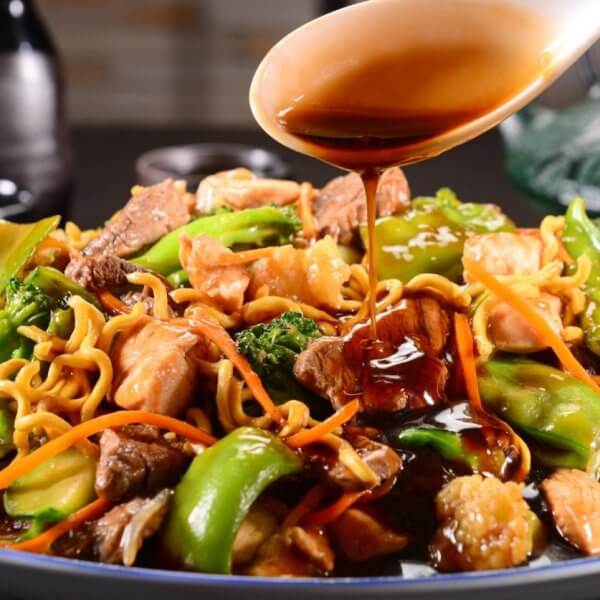 A plate of stir-fried noodles with beef, chicken, broccoli, and bell peppers being topped with soy sauce provides a mouth-watering experience. You can savor this delectable dish at one of the best restaurants in Robinsons Galleria.