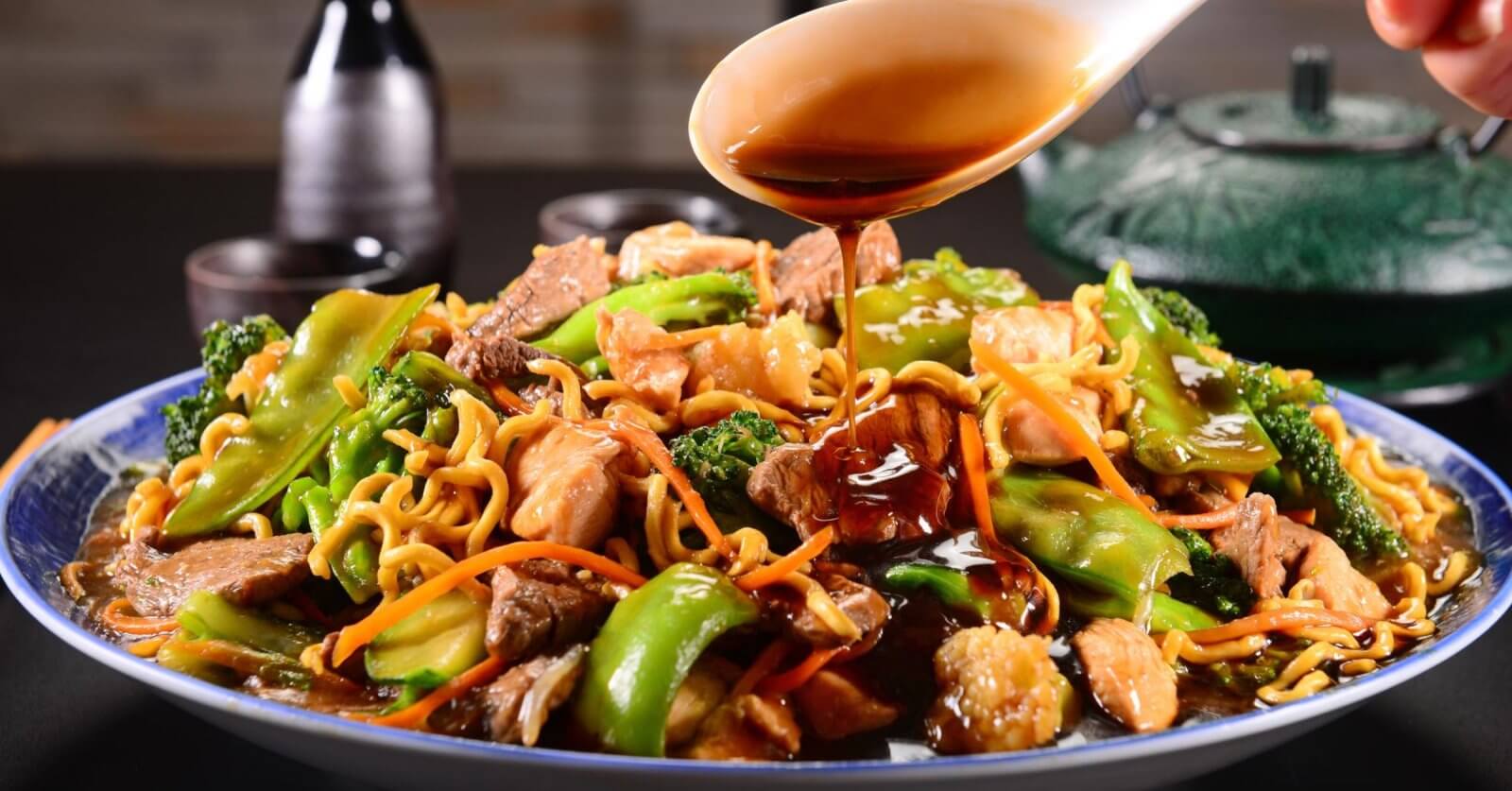 A plate of stir-fried noodles with beef, chicken, broccoli, and bell peppers being topped with soy sauce provides a mouth-watering experience. You can savor this delectable dish at one of the best restaurants in Robinsons Galleria.