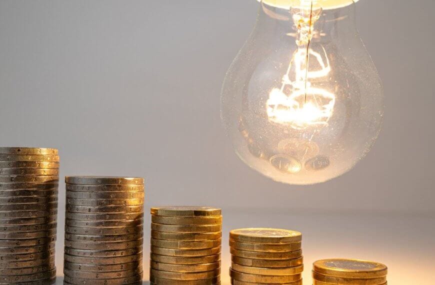Stacked coins beneath a lit bulb, symbolizing electric consumption and the potential to save with solar.